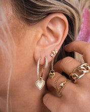 Blonde girl with several ear piercings wearing hoops and studs with dangling charms and stacking gold rings that are water resistant
