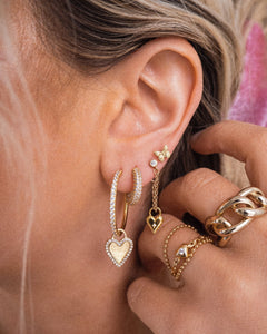 Blonde girl with several ear piercings wearing hoops and studs with dangling charms and stacking gold rings that are water resistant